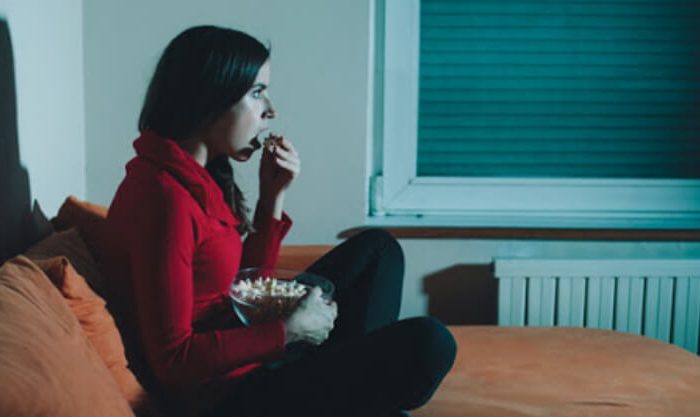 Mulher a comer pipocas enquanto vê uma série