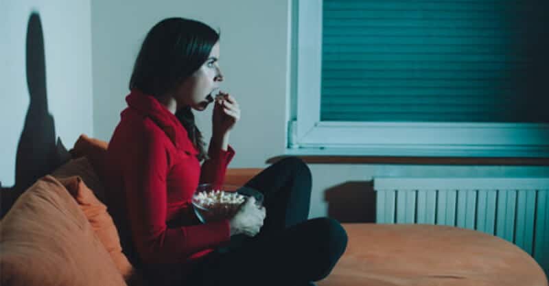 Mulher a comer pipocas enquanto vê uma série